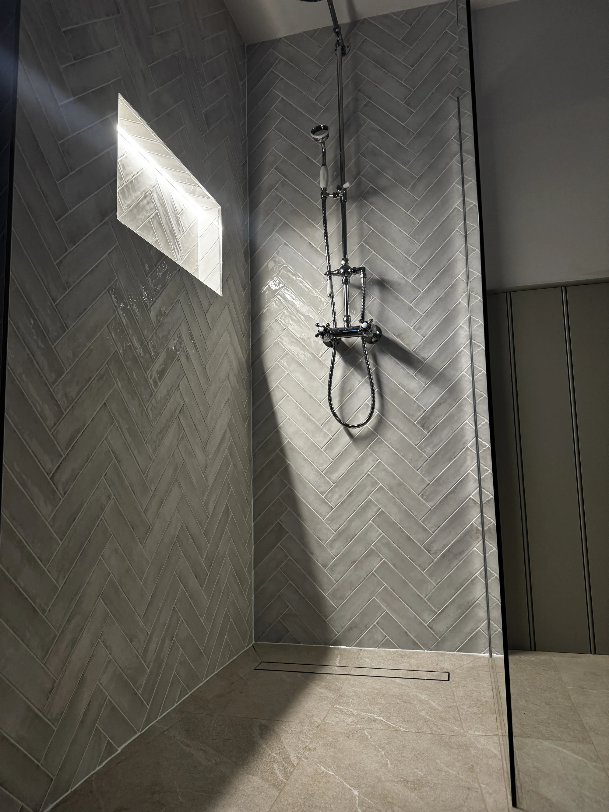 Walk-in shower lined in herringbone stone-look tile with a lit niche, Baldock