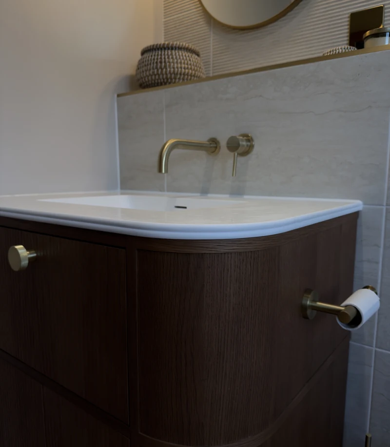 Wall-mounted brass taps over the curved countertop basin, Weston